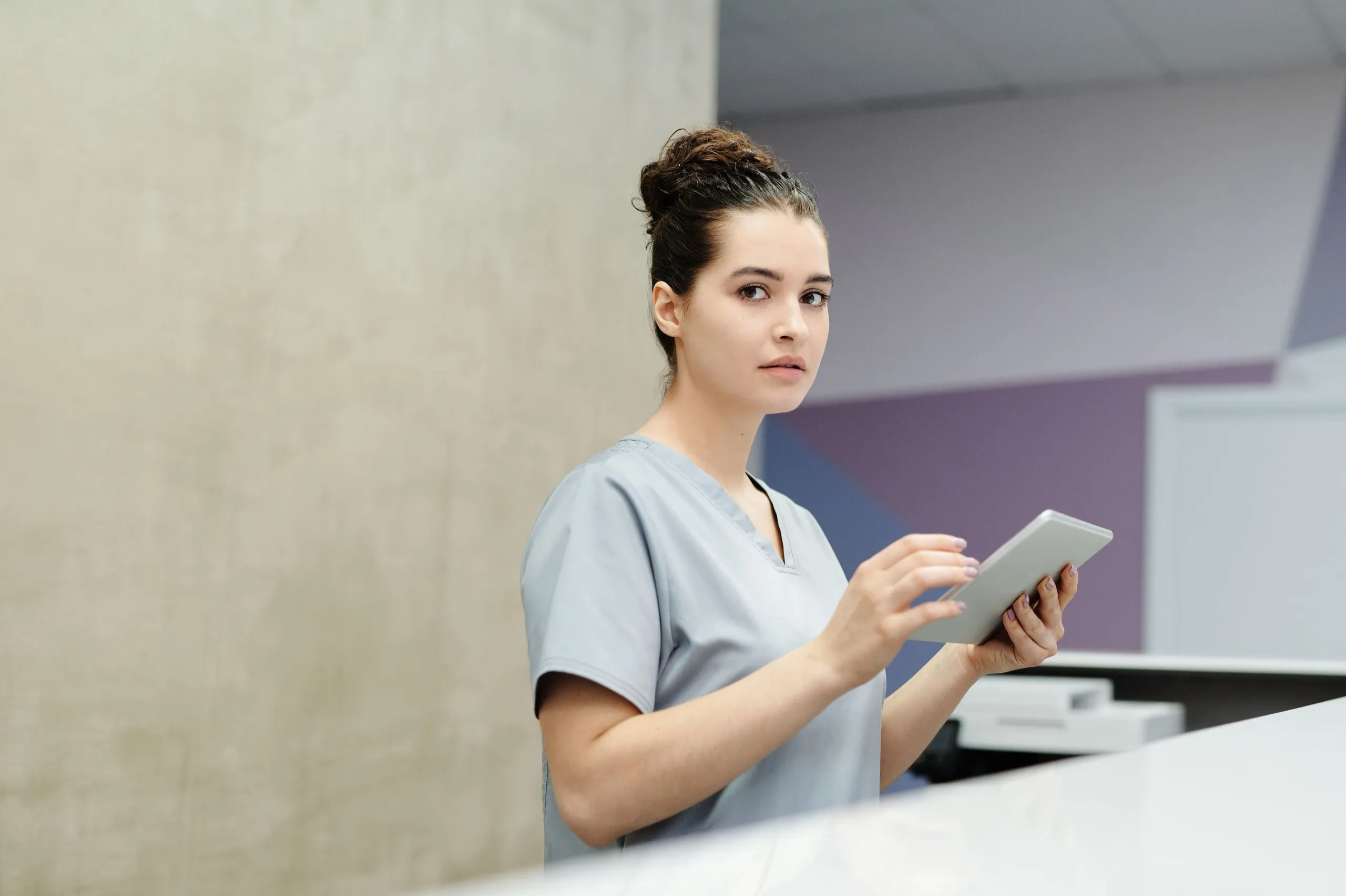 A clinic receptionist holds a tablet at the front desk