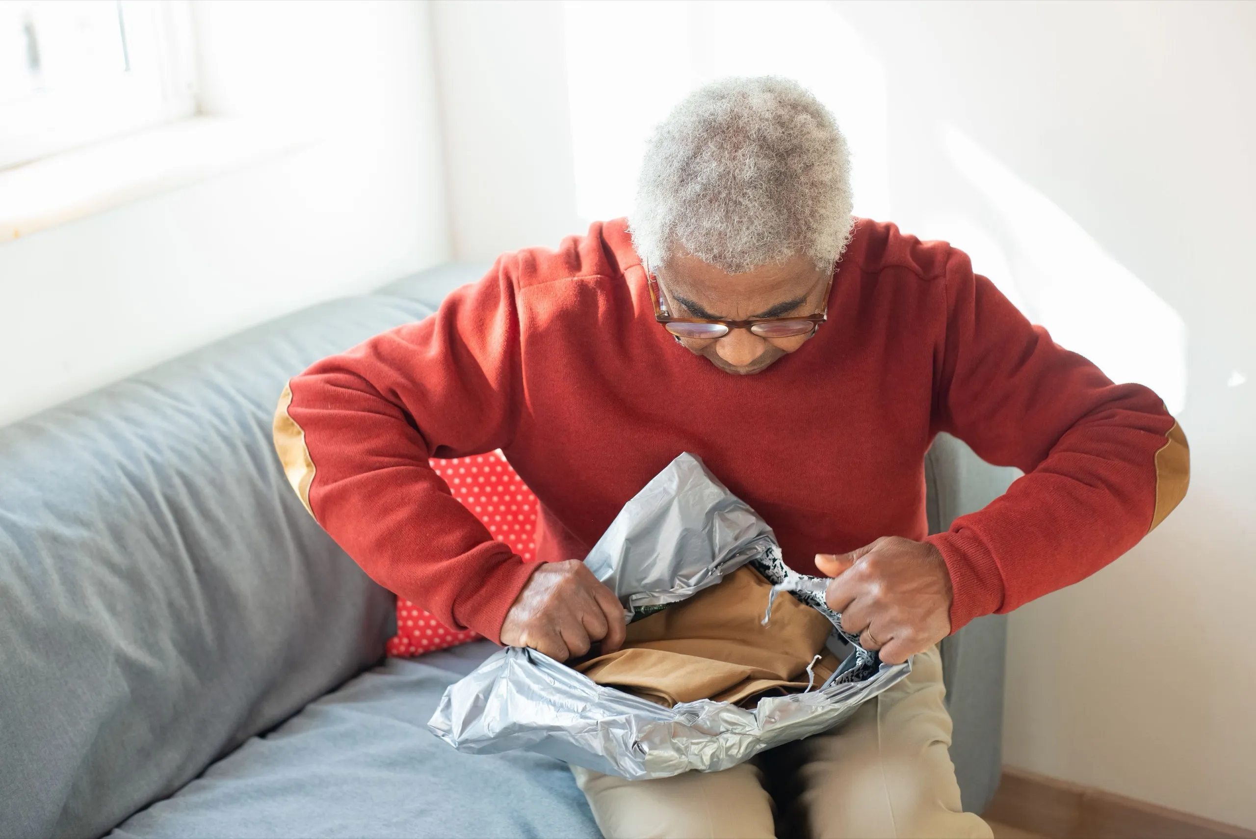 An older man opens a delivery package on his sofa